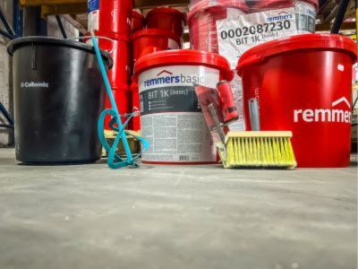 Rote Eimer mit Malerwerkzeug wie Pinsel und R&uuml;hrstab stehen auf Boden im Lager