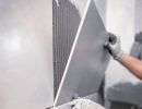 H&auml;nde mit Handschuhen setzen Wandfliesen &ndash; zeigt sorgf&auml;ltiges und pr&auml;zises Arbeiten beim Fliesenlegen im Innenbereich