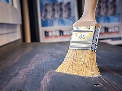 Pinsel liegt auf lasierter Holzfl&auml;che, Farbauftrag im Detail, Hinweis auf Holzschutz und Gestaltung mit Lasur