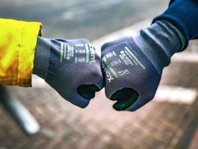 Zwei H&auml;nde mit Arbeitshandschuhen sto&szlig;en F&auml;uste zusammen, symbolisieren Teamarbeit und Arbeitsschutz