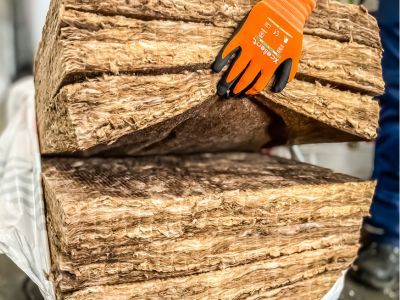 Hand mit orange Handschuh h&auml;lt Glaswolle-Isolierung, zeigt Material zur W&auml;rmed&auml;mmung von Geb&auml;uden